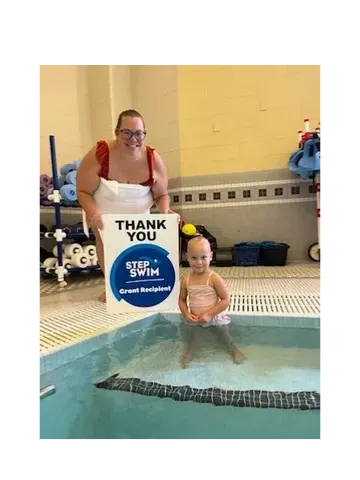 A young swimmer in the pool beside a Step Into Swim thank-you sign